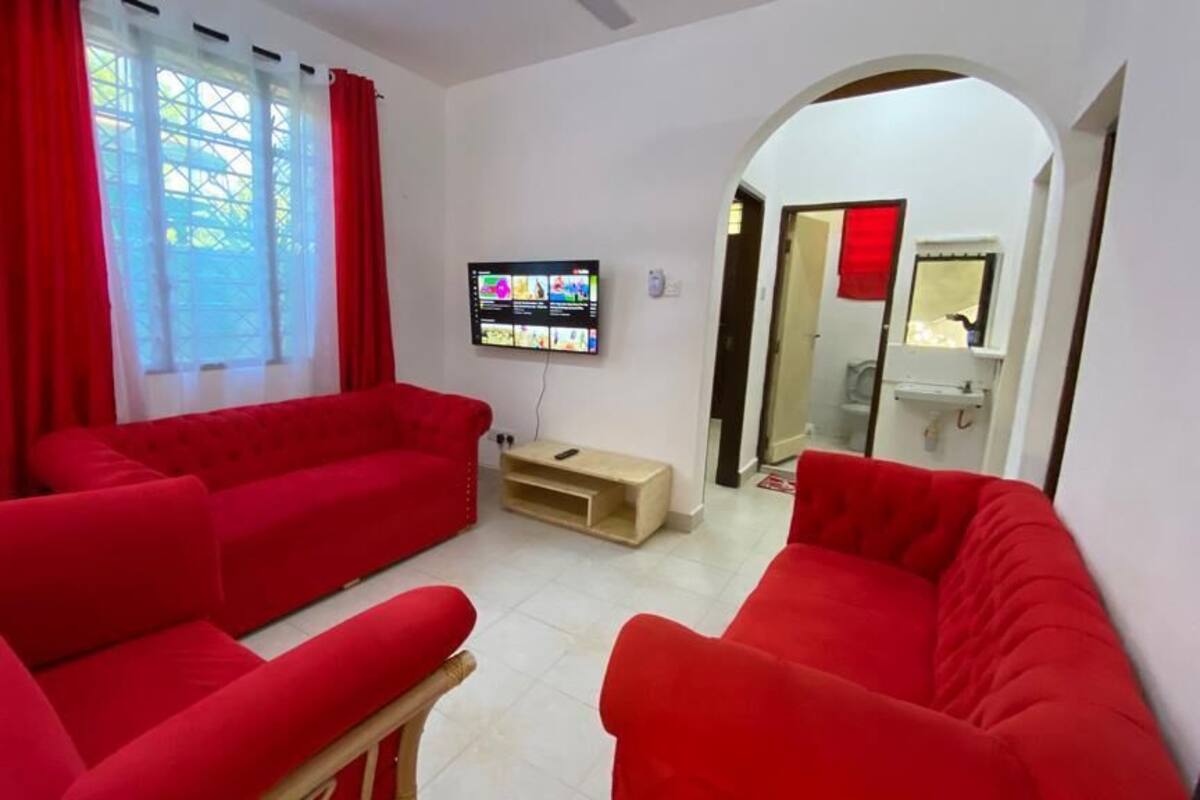A living room with red sofas, a TV mounted on the wall, and a wooden side table.