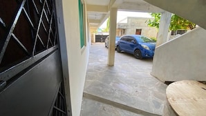 A covered outdoor area with a blue car parked in the background, a concrete staircase, and a metal gate. - Lux Suites Mtwapa Beach Road Apartments (Mtwapa)