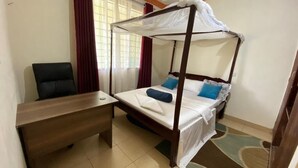 A single bed with a canopy, a wooden desk, and a chair in a room with a tiled floor and a window with curtains. - Lux Suites Mtwapa Beach Road Apartments (Mtwapa)