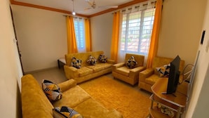 A living room with a sofa set, a TV, and a window with curtains. - Lux Suites Mtwapa Beach Road Apartments (Mtwapa)