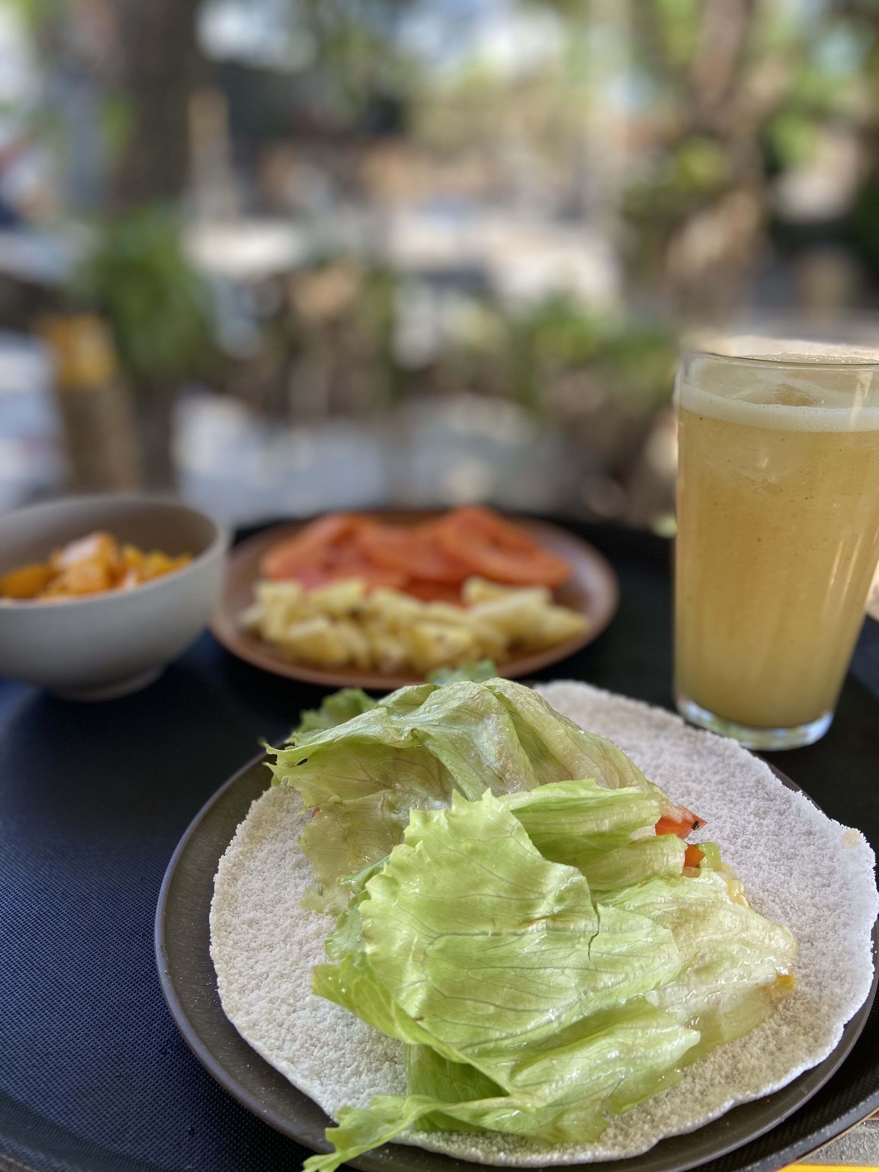 A meal with lettuce on a plate, a glass of beverage, and a bowl of food in the background.