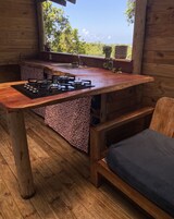 Interior em madeira com cozinha, incluindo fogão a gás, pia e janela com vista para a paisagem natural.