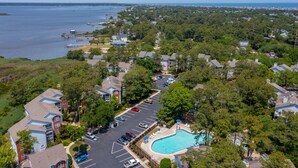 An aerial view of a residential area with a swimming pool, parking lot, and waterfront. - Clean & Modern - 4 guests - Pool & Tennis (Kill Devil Hills)