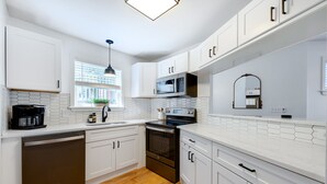 A modern kitchen with white cabinets, a microwave, an oven, and a coffee maker. - Clean & Modern - 4 guests - Pool & Tennis (Kill Devil Hills)