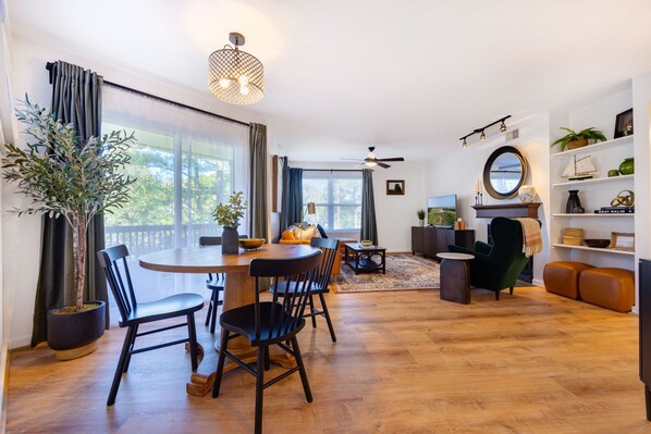 A modern living room with a dining area, large windows, and a ceiling fan. - Clean & Modern - 4 guests - Pool & Tennis (Kill Devil Hills)
