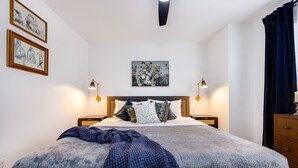 A neatly arranged bedroom with a large bed, two bedside tables, a headboard, and a wall-mounted artwork. - Clean & Modern - 4 guests - Pool & Tennis (Kill Devil Hills)