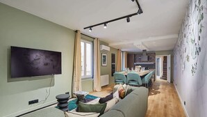 A modern living room with a flat-screen TV, a sofa, a dining area with a table and chairs, and a staircase leading to another level. - Sublime triplex Paris Le Marais (Paris)