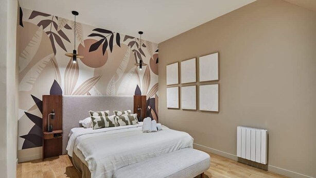 A bedroom with a bed, bedside tables, a radiator, and a wall with framed artwork. - Sublime triplex Paris Le Marais (Paris)