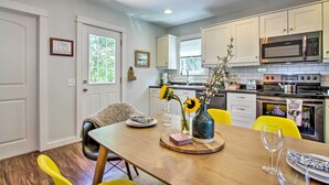 A modern kitchen with white cabinets, a built-in microwave, and a stove. There is a dining table with yellow chairs and a vase with sunflowers.