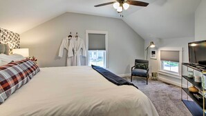 Un dormitorio con una cama grande, ventilador de techo, ventana con persianas, una silla y un mueble para televisor.