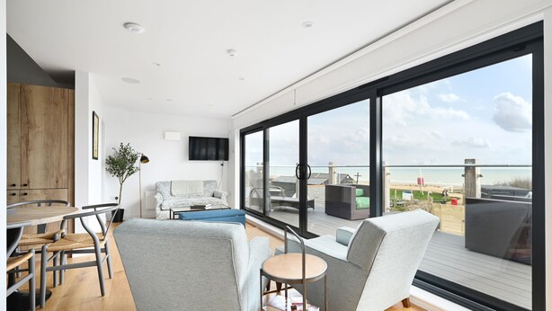 A modern living room with a large window, a dining area, and a view of the beach.