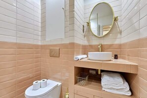 A bathroom with beige and white tiles, a white sink, a gold-framed mirror, and a toilet with two rolls of toilet paper. - Superb apartment with AC - Beaubourg Le Marais (Paris)