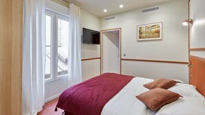 A hotel room with a bed, a television mounted on the wall, a painting, and a window with curtains. - Superb apartment with AC - Beaubourg Le Marais (Paris)