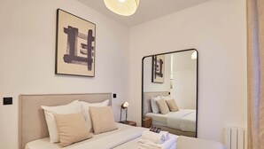A neatly made bed with a headboard, a bedside lamp, and a mirror on the wall. - Charming & Modern apartment  center of Paris (Paris)