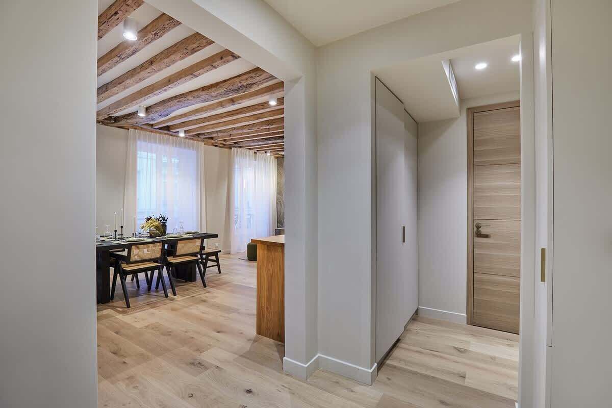 Un intérieur moderne avec un coin repas, des poutres en bois au plafond et un plancher de couleur claire.