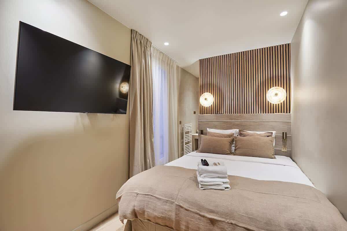 A modern hotel room with a large bed, a flat-screen TV mounted on the wall, and a wooden panel design on the headboard.