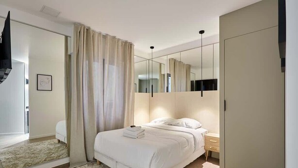 A modern bedroom with a large bed, a wardrobe, a mirror, and a ceiling light. - Modern Parisian apartment  Center of Paris (Paris)