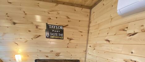 A wooden cabin room with a bed, a nightstand, and a sign that reads "TAYLOR PORT TASTE THE DIFFERENCE".