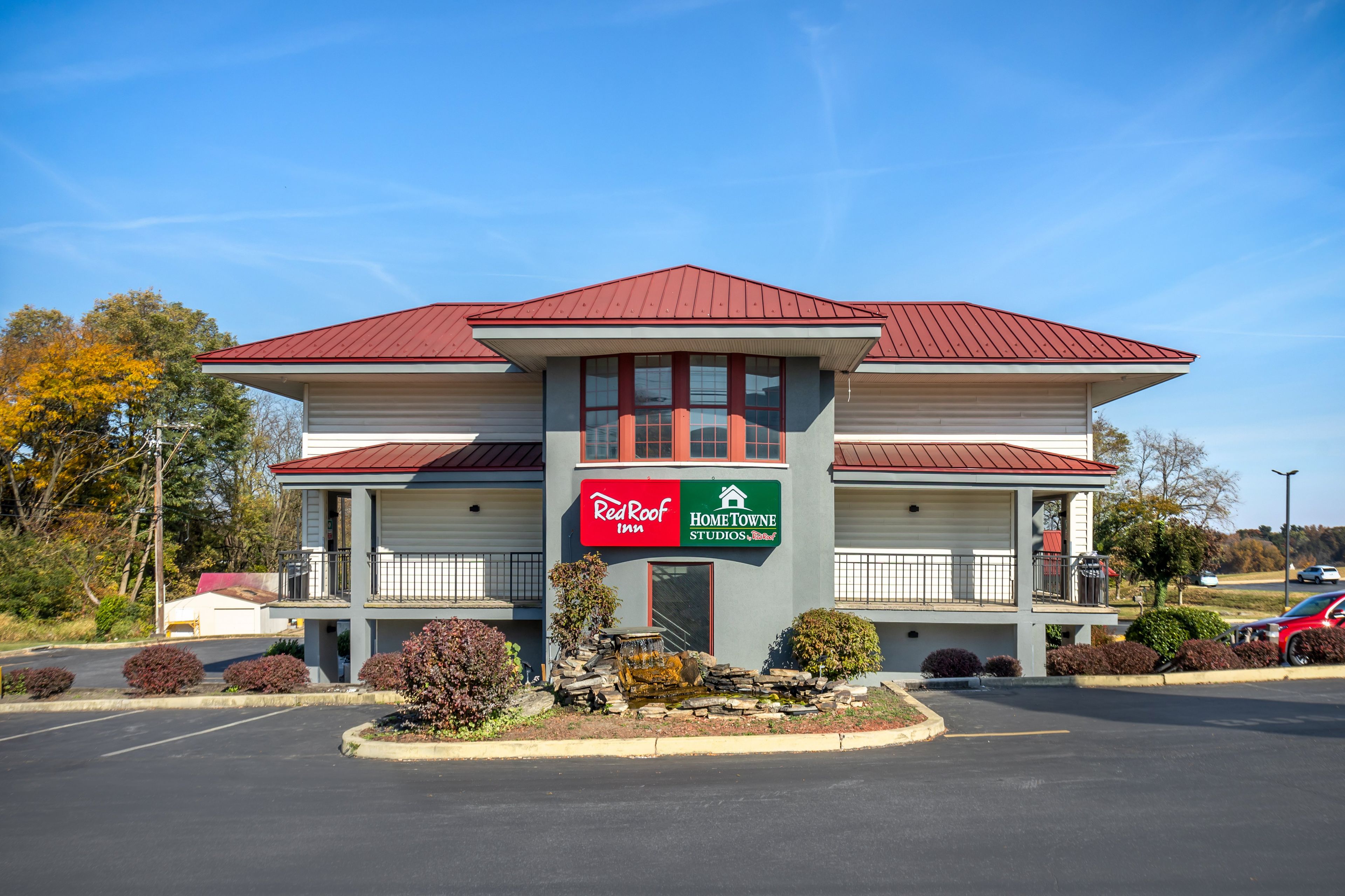 Um edifício de dois andares com telhado vermelho e uma placa indicando Red Roof Inn e Hometown Studios.