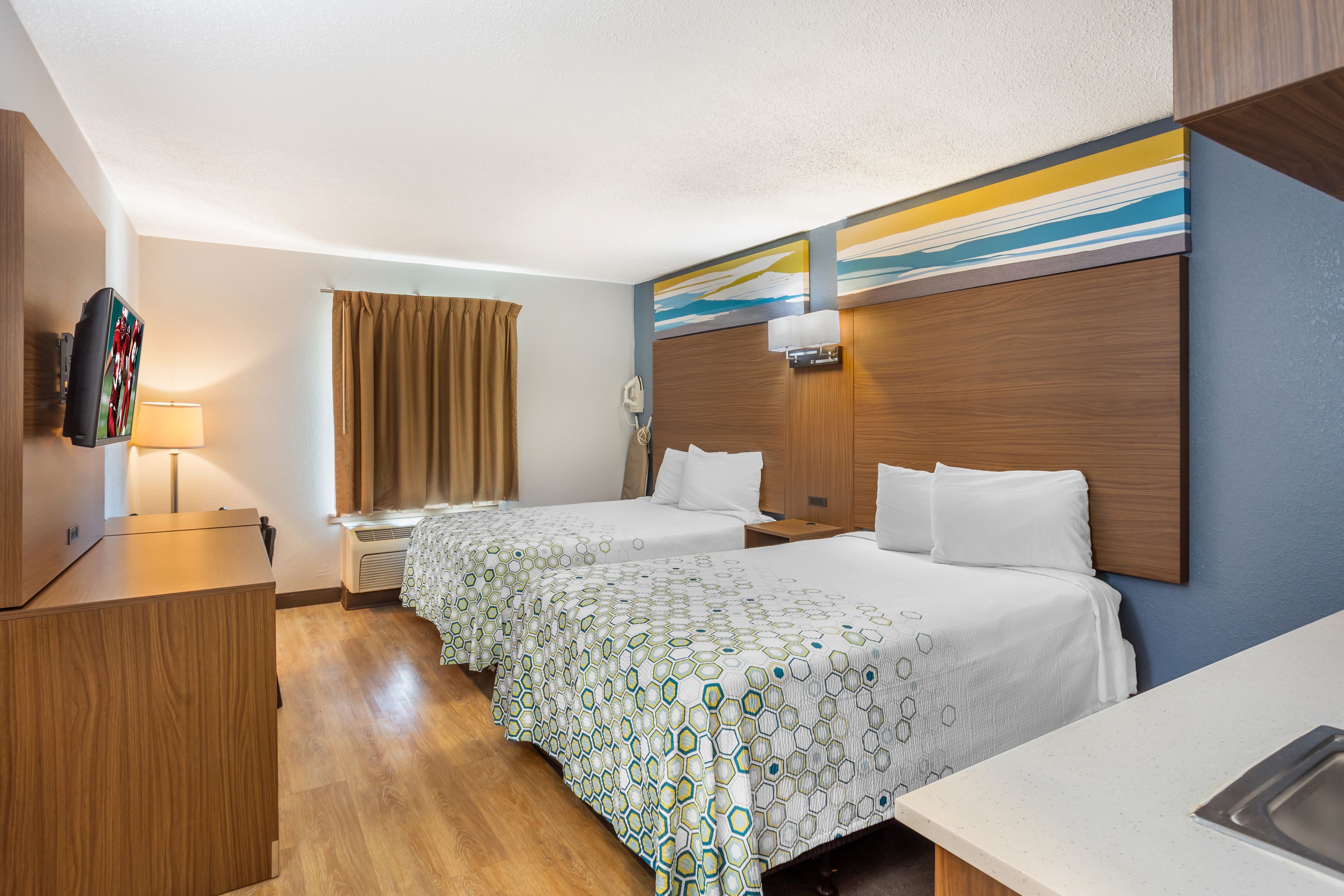 A hotel room with two beds, a desk, a TV, and a bathroom.