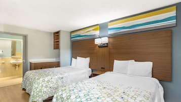 Quarto de hotel com duas camas, uma cabeceira de madeira, banheiro com pia e espelho, e parede com arte abstrata.