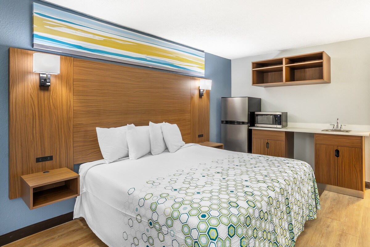 Una habitación de hotel con una cama grande, un cabecero de madera, un escritorio empotrado con microondas y un mueble pequeño de madera.