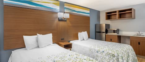 A hotel room with two beds, a wooden headboard, a small desk, a refrigerator, and a built-in shelf above the counter.