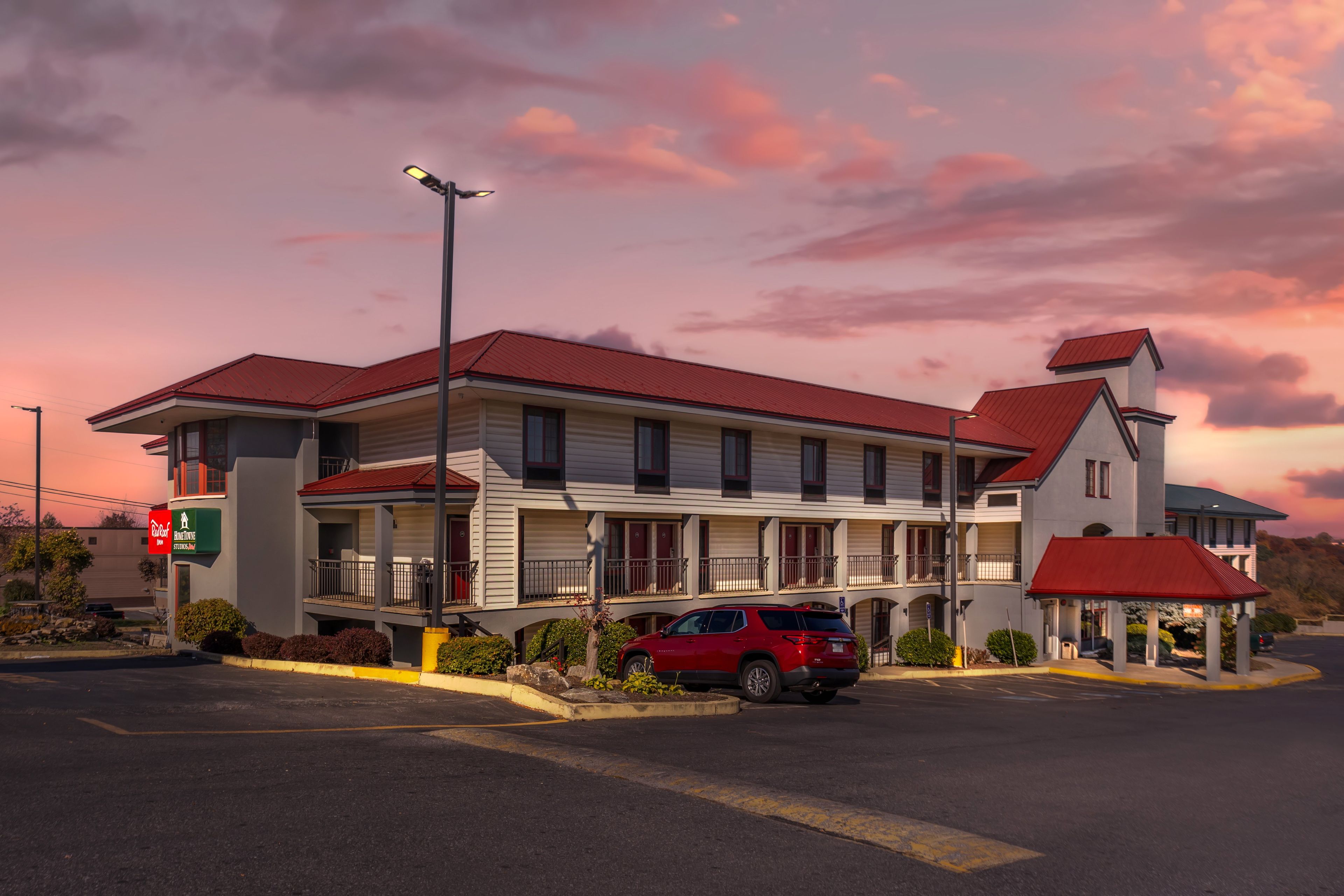 Et motel med rødt tag, flere balkoner og en parkeringsplads.