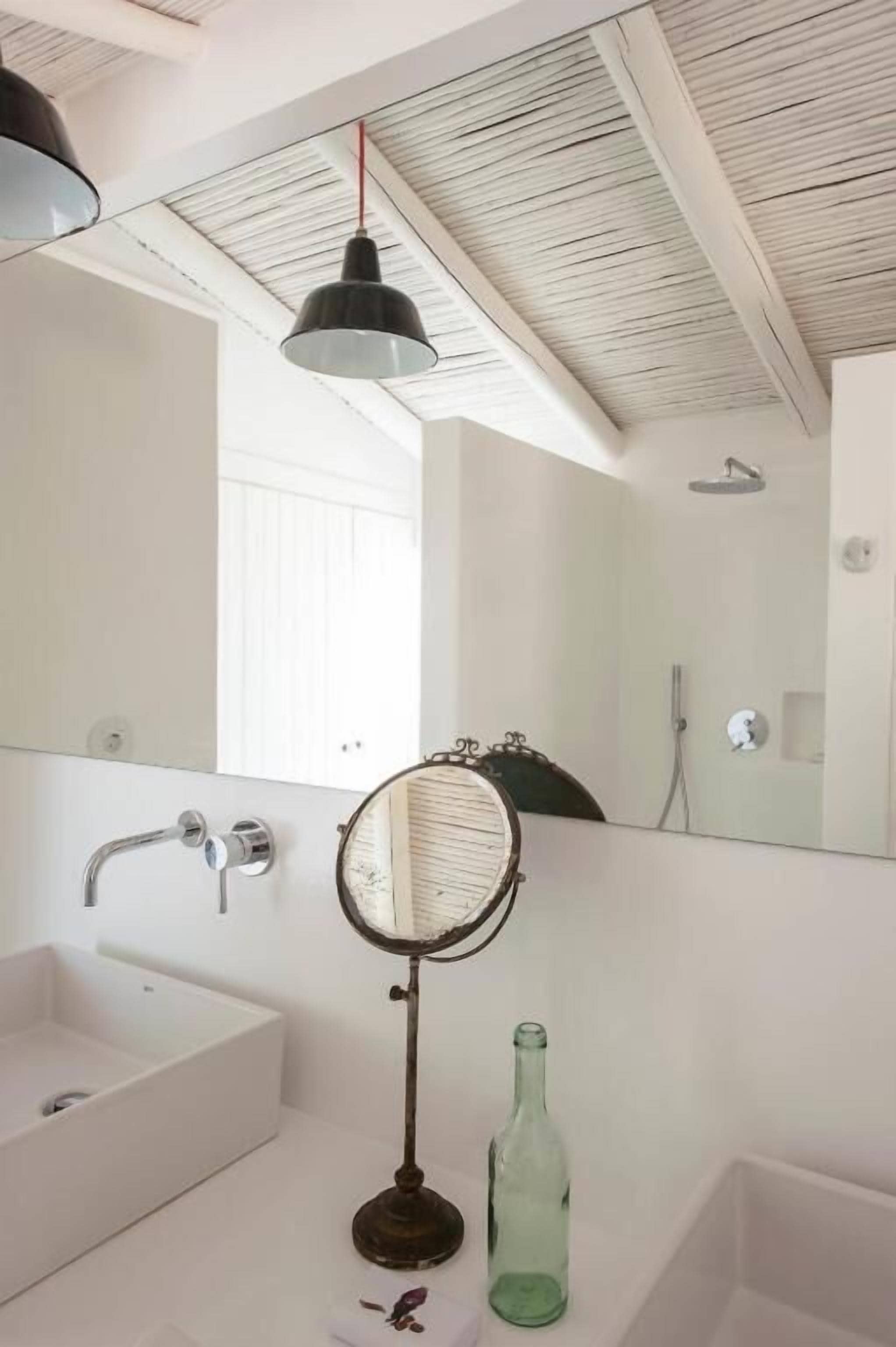 A bathroom with a large mirror, a sink, a shower, and a hanging pendant light.