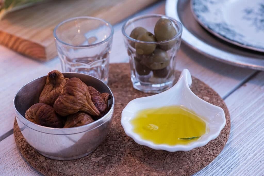 A table setting with a bowl of figs, a small glass of olive oil, and a glass of water.