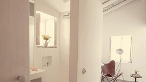 A modern, minimalist bathroom with a large mirror, a sink, and a potted plant. - Pensão Agrícola (Tavira)