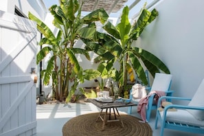 A cozy outdoor seating area with a round woven table, blue chairs, and lush banana plants. - Pensão Agrícola (Tavira)
