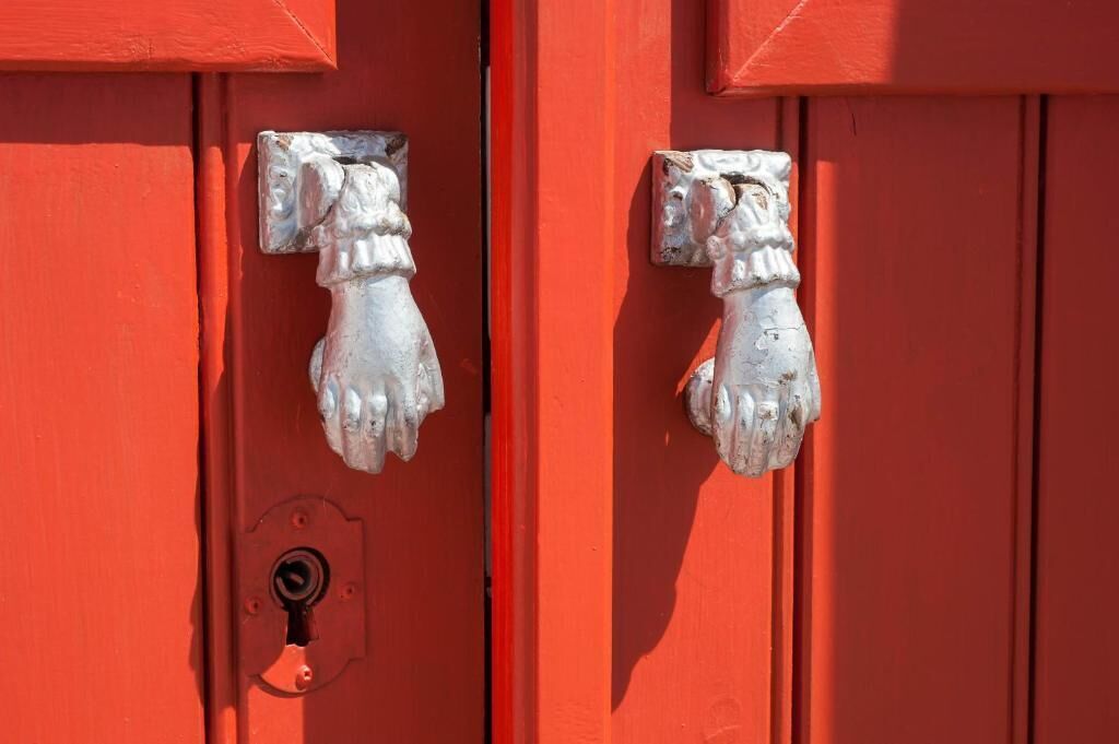 Una porta rossa con due maniglie di metallo per bussare.