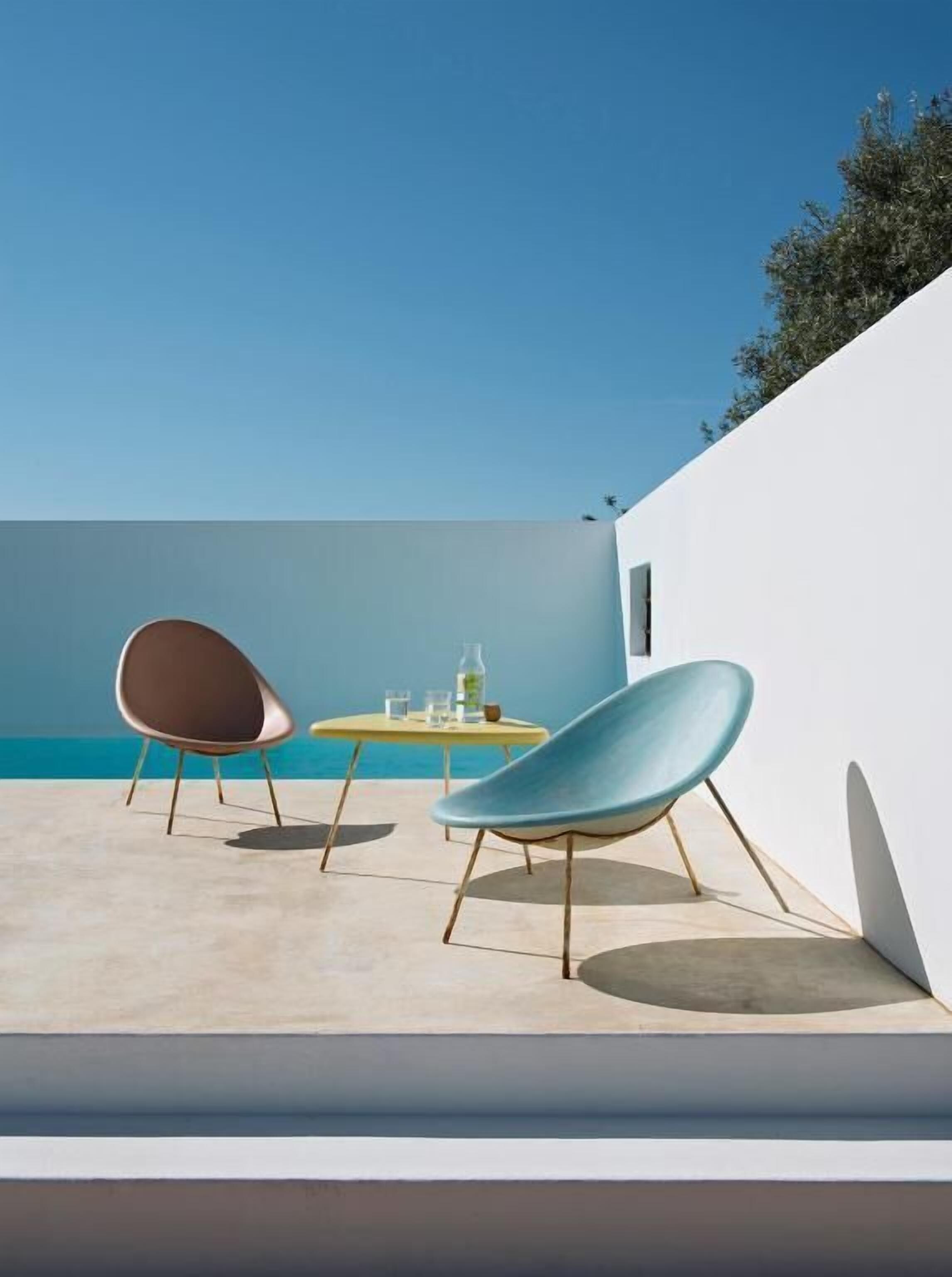 A modern outdoor seating area with two chairs and a small table, overlooking a clear blue sky and a body of water.