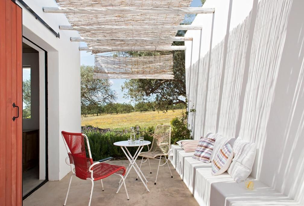 Ein überdachter Außenbereich mit weißen Sofas und roten Stühlen, einem kleinen Tisch und Blick auf eine grüne Landschaft.