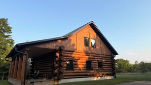 A log cabin with a porch, a chimney, and a small deck area.