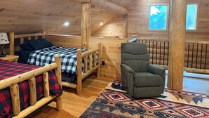 A cozy cabin interior with a loft bed, a chair, and a window.
