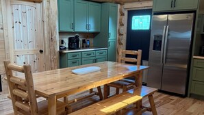 A wooden interior with a dining table, benches, and a kitchen area including a refrigerator and cabinets.