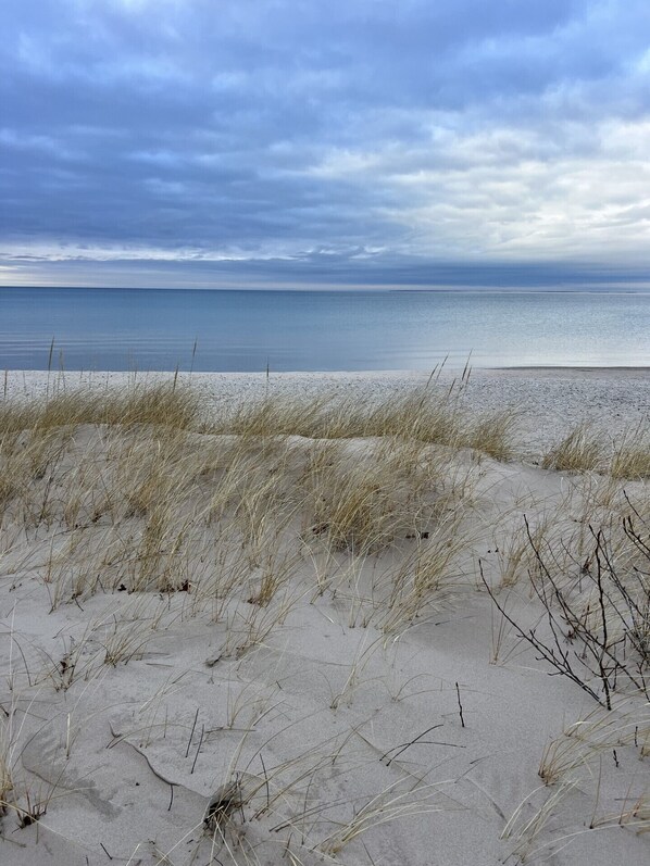 A beach with sand dunes and a calm sea under a cloudy sky.