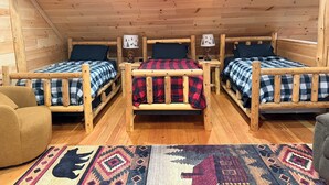 A cabin with three wooden beds, each with a checkered blanket, a nightstand, and a lamp.