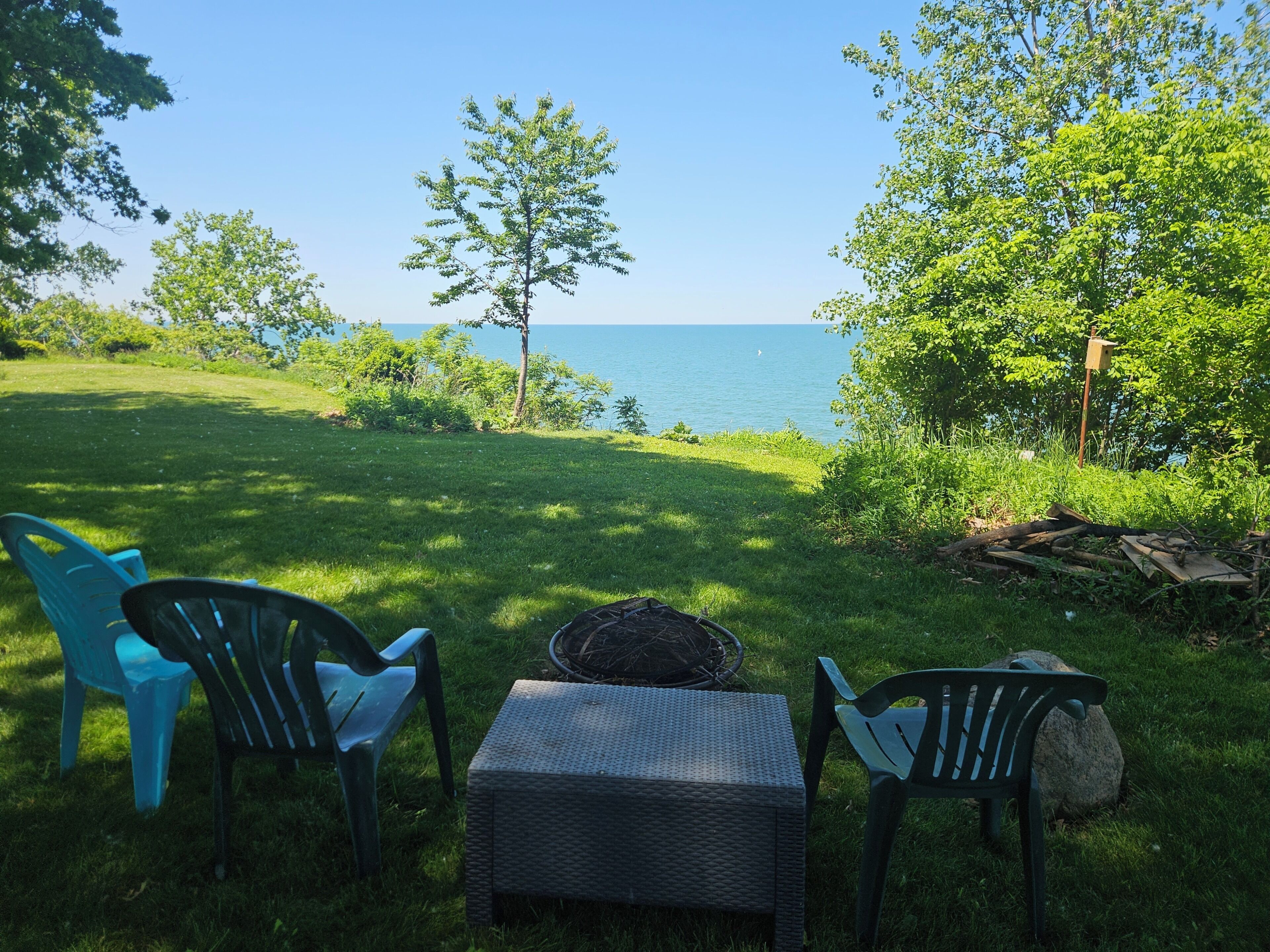 A grassy outdoor area with a view of the water, a wicker table, and two chairs.