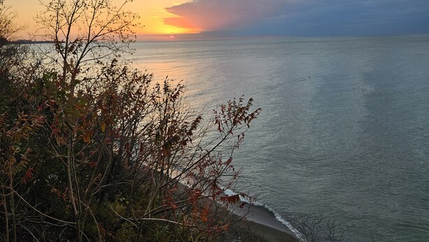 Un paysage côtier avec un coucher de soleil sur l’océan, mettant en scène une côte rocheuse et une végétation luxuriante au premier plan.