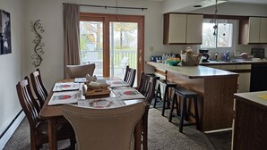 Un coin repas avec une table dressée pour quatre personnes, un ventilateur de plafond et une vue sur l’extérieur à travers une porte vitrée.