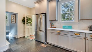 Una cocina moderna con gabinetes grises, un refrigerador de acero inoxidable y una ventana con vistas a árboles.