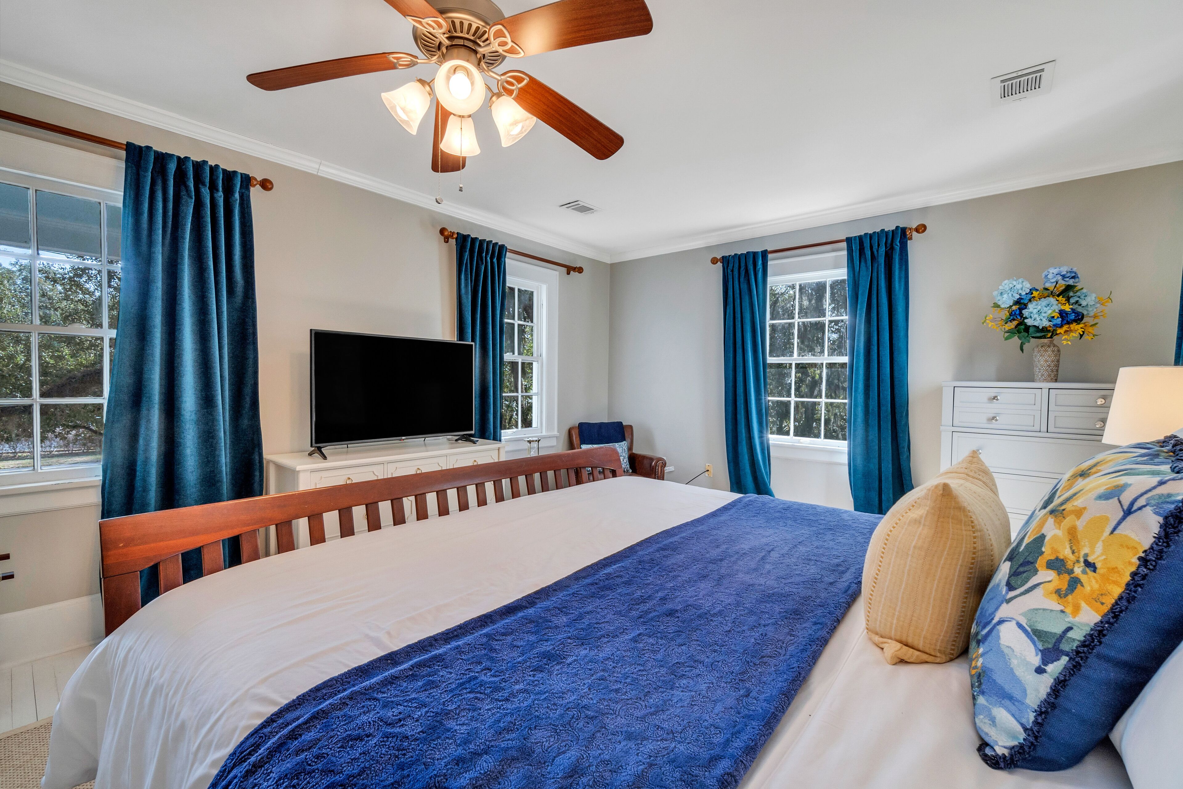 Ein Schlafzimmer mit einem großen Bett, einem Deckenventilator, einem Fernseher und einer Kommode.