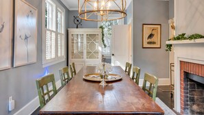 Un comedor con una mesa de madera, sillas, una araña y una chimenea.