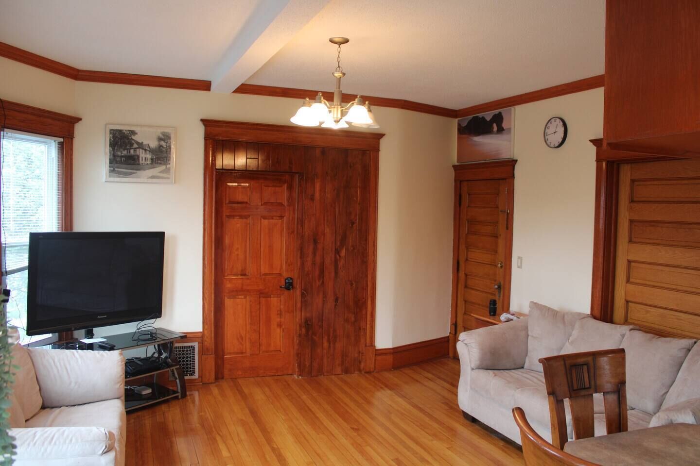 Una sala de estar con televisor, puertas de madera, sofá y candelabro.