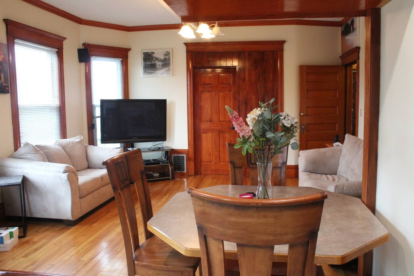 A living room with a wooden dining table, two sofas, a TV, and a vase with flowers.