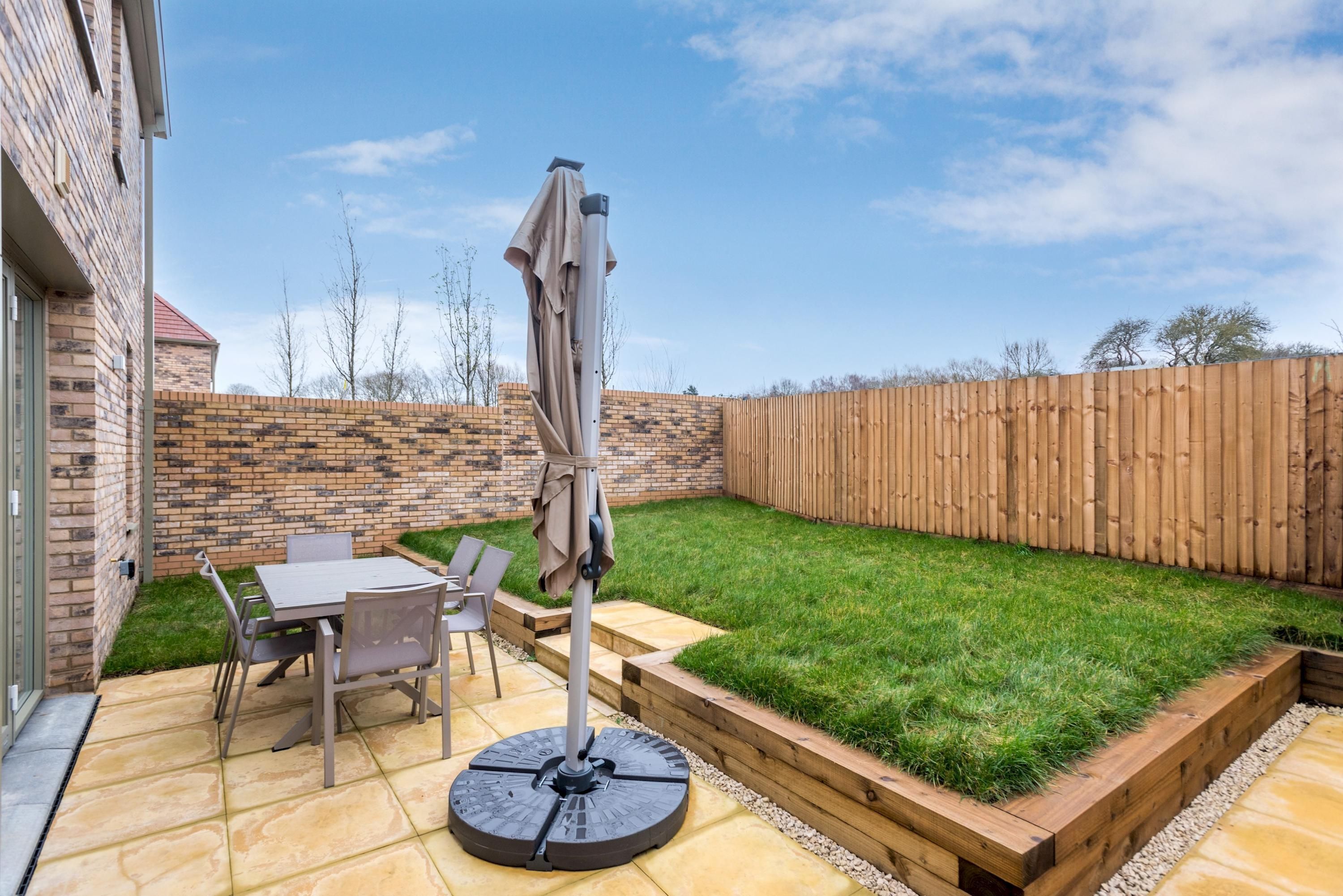 A patio with a table and chairs, a round table with a sunshade, and a wooden deck with a grassy area.