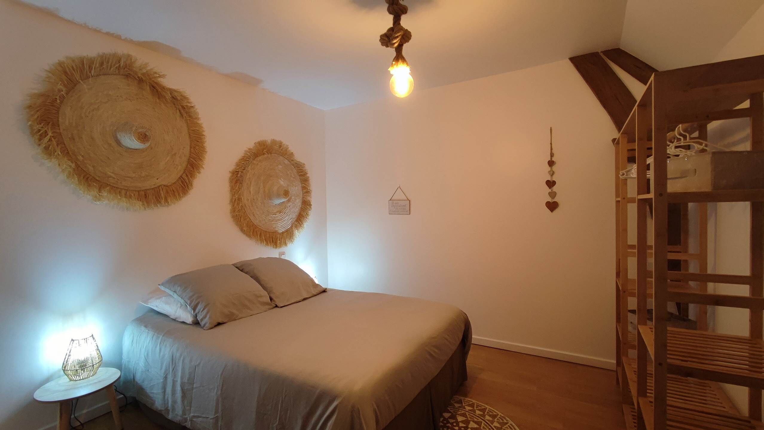 Ein Schlafzimmer mit einem Bett, einer Nachttischlampe, einer Pendelleuchte und einer an der Wand befestigten Holzleiter.